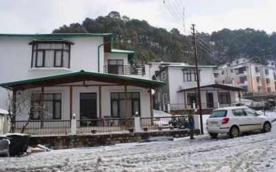 Cottage buildings during a snowfall with a car parked on a snowy road